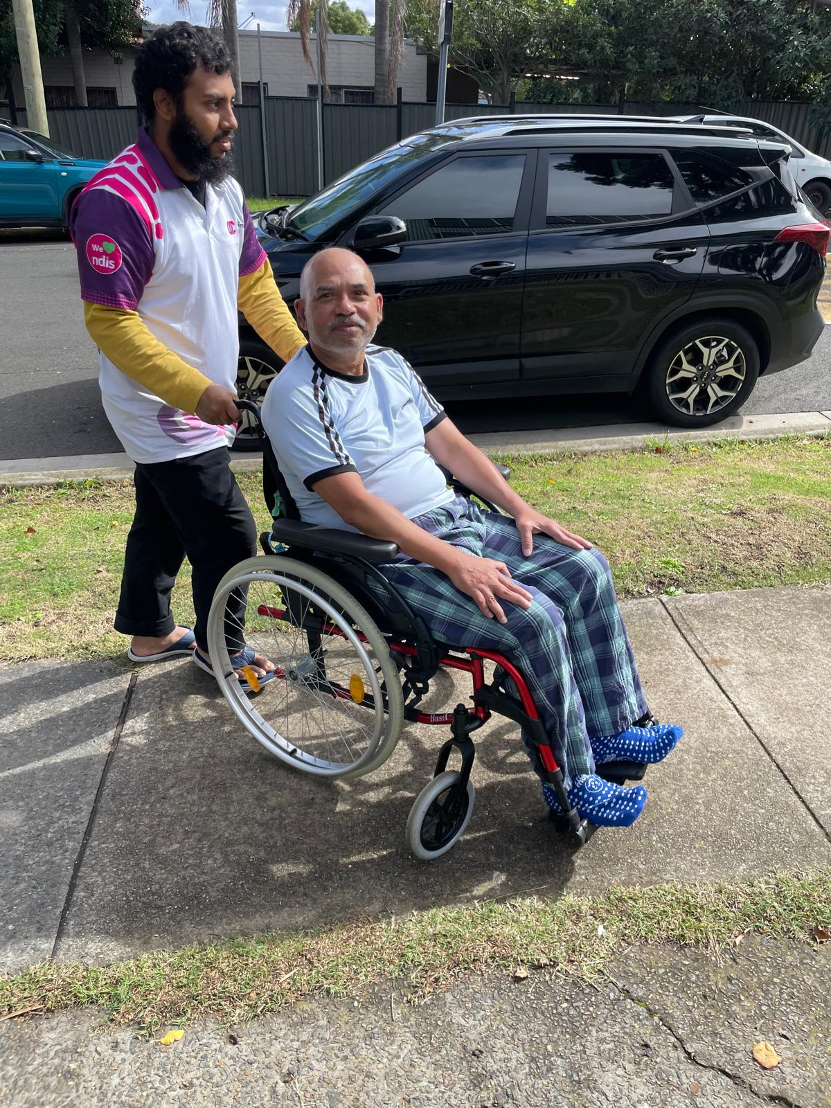 Support worker walking beside a participant in a wheelchair on the way to the car